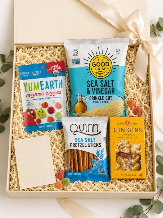 The Little Treat gift box, open — YumEarth organic fruit gummies, The Good Crisp sea salt and vinegar chips, Quinn sea salt pretzel sticks and Gin Gins ginger chews in a cream box with an ivory ribbon