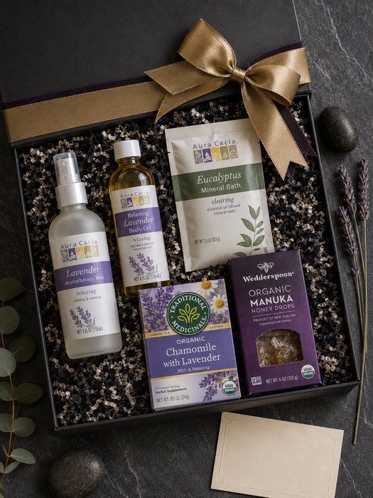 The Unplugged Evening gift box, open — Aura Cacia lavender mist, body oil and eucalyptus mineral bath, Traditional Medicinals chamomile tea and Wedderspoon manuka honey drops in a charcoal box with a gold ribbon